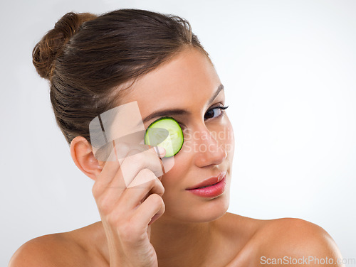 Image of Eye treatment, homestyle. Portrait of a gorgeous young woman holding a slice of cucumber over her eye.