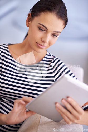 Image of The web at your fingertips. A beautiful young woman using a tablet on her couch.
