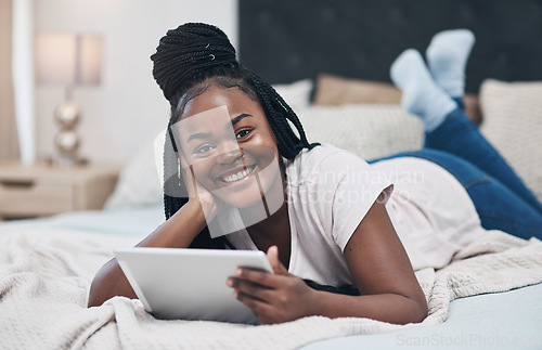 Image of My social network is keeping me company today. a young woman using a digital tablet while relaxing on her bed at home.