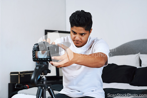 Image of I have to get the perfect angle. a young man using a camera on a tripod to record himself at home.