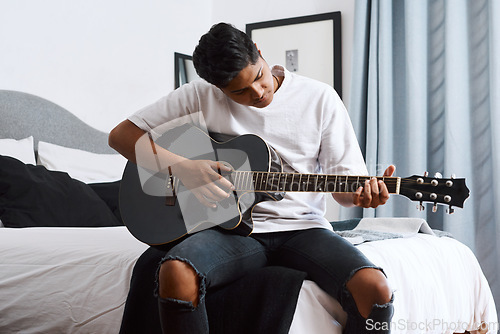 Image of Im playing my favourite song. a young man playing the guitar while sitting at home.