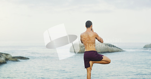 Image of Quiet the mind and the soul shall speak. Rearview shot of an unrecognizable man standing and doing yoga alone by the ocean during an overcast day.