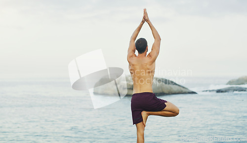 Image of Yoga is the science of well being. Rearview shot of an unrecognizable man standing and doing yoga alone by the ocean during an overcast day.