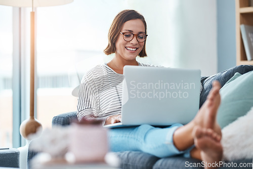 Image of She cant hide the blush on her face. Full length shot of a happy young woman using a laptop while relaxing in her living room.