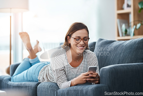 Image of Somebodys texting her crush. Full length shot of a happy young woman using her smartphone on the sofa at home.