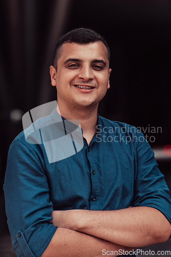 Image of A successful young businessman in a shirt, with crossed arms, poses outdoors, confident expression on his face.