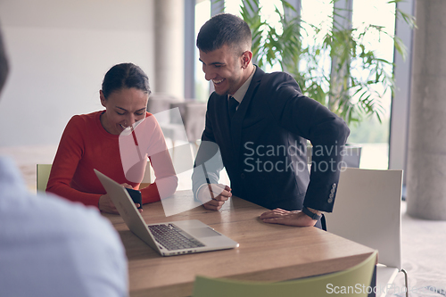 Image of A young entrepreneurial couple sits together in a large, modern office, engaged in analyzing statistics and data on their laptop