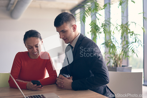 Image of A young entrepreneurial couple sits together in a large, modern office, engaged in analyzing statistics and data on their laptop