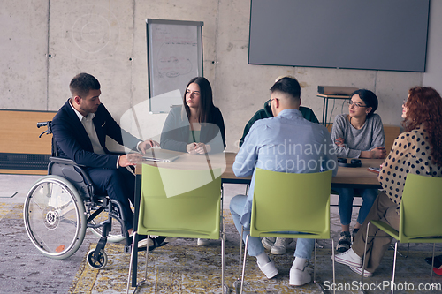 Image of A diverse group of business professionals, including an person with a disability, gathered at a modern office for a productive and inclusive meeting.