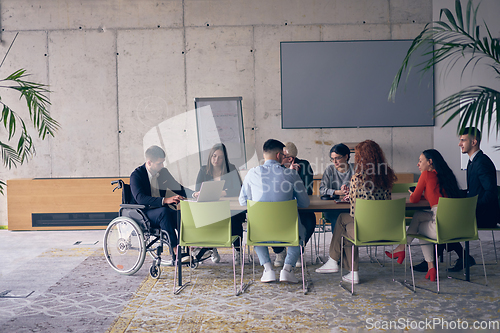 Image of A diverse group of business professionals, including an person with a disability, gathered at a modern office for a productive and inclusive meeting.