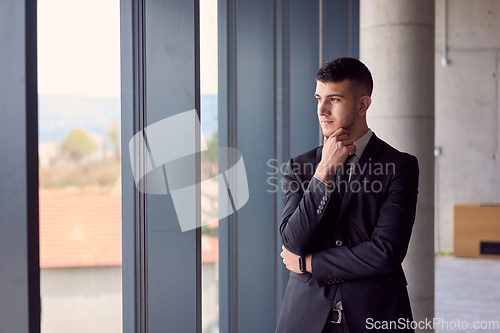 Image of The confident businessman in a sleek suit strikes a pose, exuding charisma and professionalism, amidst the modern ambiance of the office.