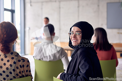 Image of A young hijab woman entrepreneur is attentively listening to a presentation by her colleagues, reflecting the spirit of creativity, collaboration, problem-solving, entrepreneurship, and empowerment.