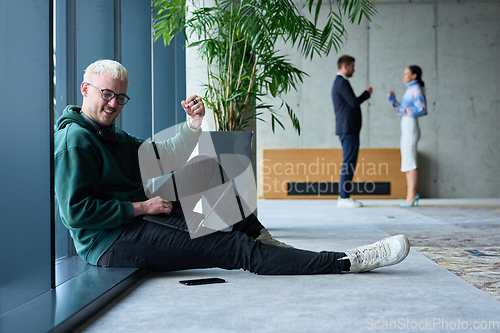 Image of A young blond man in a modern office sits by the window, engrossed in his work on a laptop