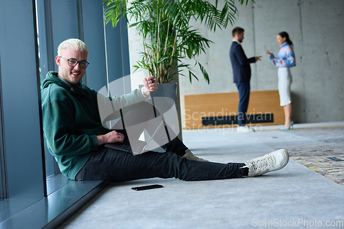 Image of A young blond man in a modern office sits by the window, engrossed in his work on a laptop