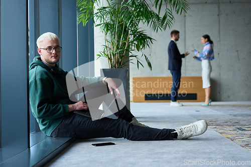 Image of A young blond man in a modern office sits by the window, engrossed in his work on a laptop