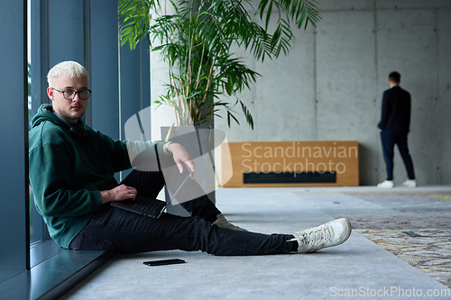 Image of A young blond man in a modern office sits by the window, engrossed in his work on a laptop