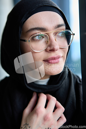 Image of A hijab businesswoman stands by the window in a modern office holding a tablet in her hand showcasing her professionalism, technological prowess and entrepreneurial spiri