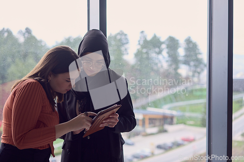 Image of In a modern office a pair of colleagues, one wearing a hijab, engage in a lively discussion, sharing their business ideas and fostering a diverse and inclusive work environment.