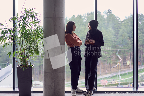 Image of In a modern office a pair of colleagues, one wearing a hijab, engage in a lively discussion, sharing their business ideas and fostering a diverse and inclusive work environment.