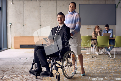 Image of A businessman in a wheelchair and his female colleague together in a modern office, representing the power of teamwork, inclusion and support, fostering a dynamic and inclusive work environment.