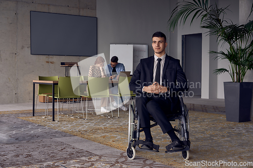 Image of Businessman in a wheelchair commands attention, symbolizing resilience and success amidst a dynamic modern office environment.