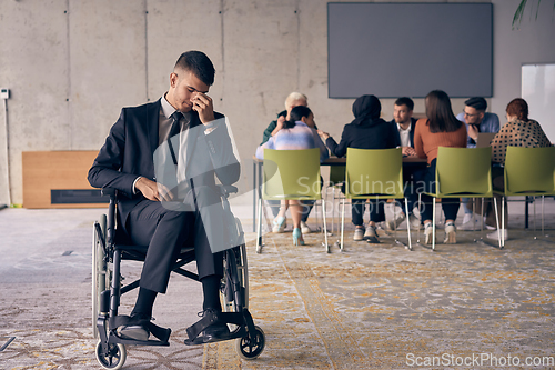 Image of A melancholic businessman in a wheelchair sitting with a sad expression, gazing through the window of a modern office, conveying a sense of solitude