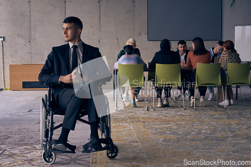 Image of Businessman in a wheelchair commands attention, symbolizing resilience and success amidst a dynamic modern office environment.