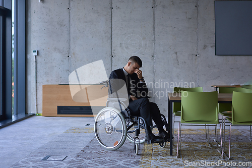 Image of A melancholic businessman in a wheelchair sitting with a sad expression, gazing through the window of a modern office, conveying a sense of solitude