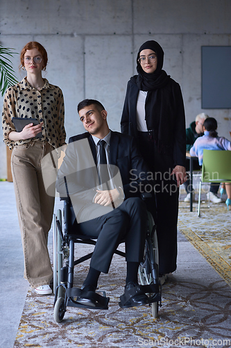 Image of A businessman with disability in a wheelchair is surrounded by supportive colleagues in a modern office, showcasing the strength of teamwork, inclusivity, and empowerment in the face of challenges.