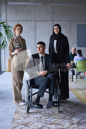 Image of A businessman with disability in a wheelchair is surrounded by supportive colleagues in a modern office, showcasing the strength of teamwork, inclusivity, and empowerment in the face of challenges.