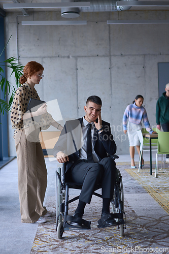 Image of A businessman in a wheelchair and his female colleague together in a modern office, representing the power of teamwork, inclusion and support, fostering a dynamic and inclusive work environment.