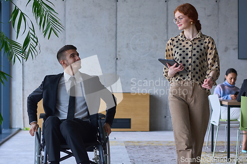 Image of A businessman in a wheelchair and his female colleague together in a modern office, representing the power of teamwork, inclusion and support, fostering a dynamic and inclusive work environment.