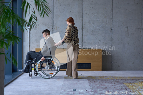 Image of A businessman in a wheelchair and his female colleague together in a modern office, representing the power of teamwork, inclusion and support, fostering a dynamic and inclusive work environment.