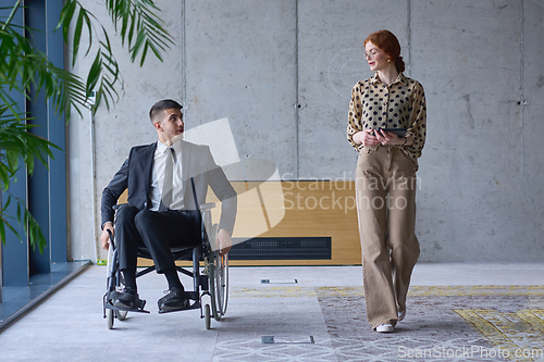 Image of A businessman in a wheelchair and his female colleague together in a modern office, representing the power of teamwork, inclusion and support, fostering a dynamic and inclusive work environment.