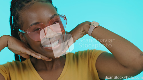 Image of Happy, heart and portrait of a black woman with sunglasses for summer on a blue background. Smile, perfect and a model or African girl with trendy eyewear, fashion and hands on face on a backdrop