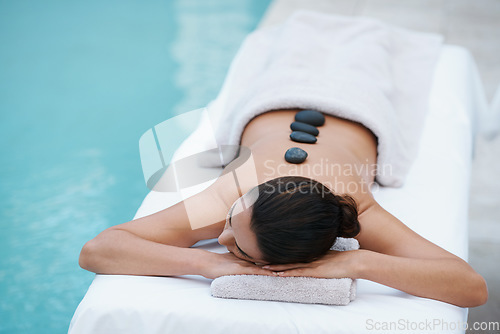 Image of Hot stone therapy taking her cares away. a beautiful woman lying on a poolside massage table.