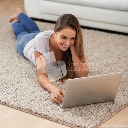 Image of Daily dose of social networking. A woman lying on her living room floor while using her laptop.