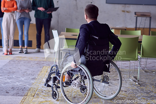 Image of A group of diverse entrepreneurs gather in a modern office to discuss business ideas and strategies, while a colleague in a wheelchair joins them.