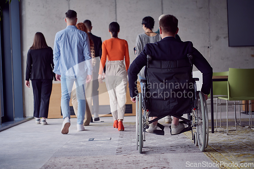 Image of A diverse group of businessmen, including a businessman in wheelchair, confidently stride together through a modern, spacious office, epitomizing collaboration, inclusivity, and strength in unity