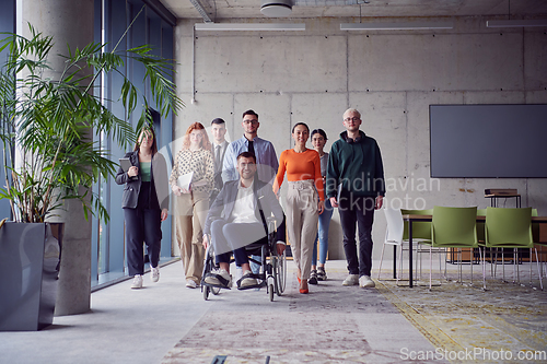 Image of A diverse group of businessmen, including a businessman in wheelchair, confidently stride together through a modern, spacious office, epitomizing collaboration, inclusivity, and strength in unity