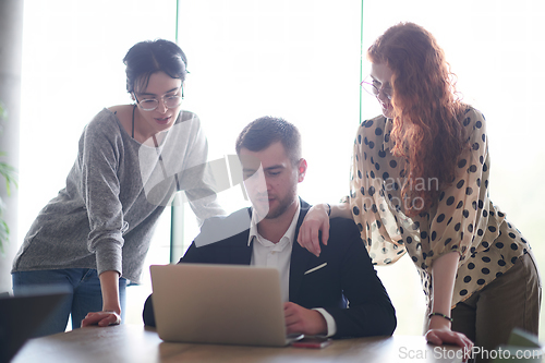 Image of A businessman engaging in a discussion about sales statistics with his two female colleagues while they examine the data on a laptop in a modern office setting