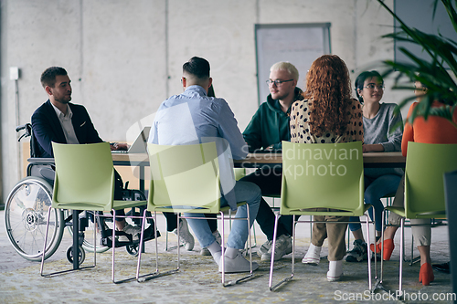 Image of A diverse group of business professionals, including an person with a disability, gathered at a modern office for a productive and inclusive meeting.