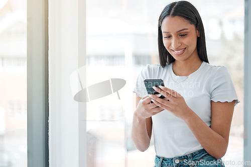 Image of Whats everyone doing tonight. an attractive young woman standing alone at home and using her cellphone.