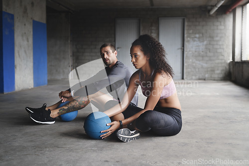 Image of Lets get the ball rolling. Full length shot of sporty young couple sitting down and exercising with a ball inside a parking lot.