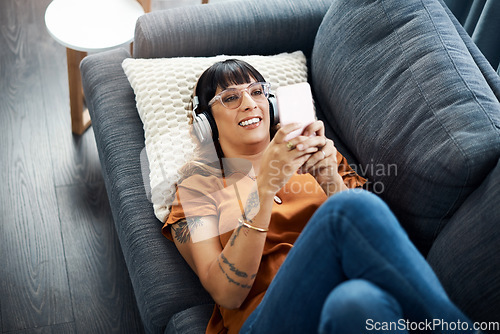 Image of Music has a relaxing effect on our minds and bodies. a young woman wearing headphones while using her cellphone at home.