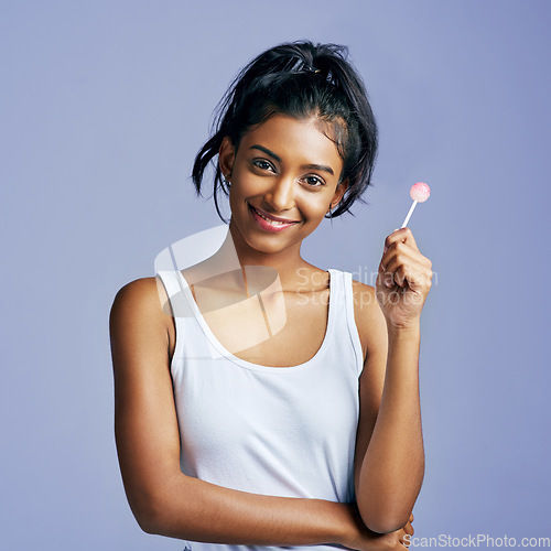 Image of Smiling sweetly. Studio portrait of a beautiful young woman sucking on a lollipop against a purple background.