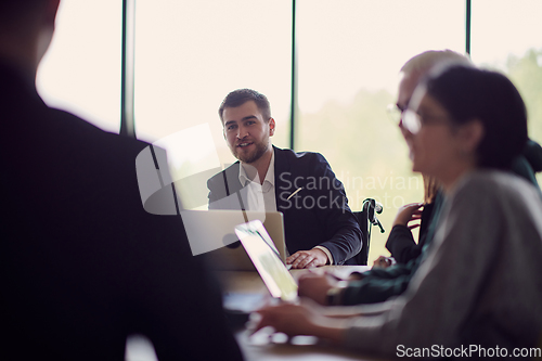 Image of A diverse group of business professionals, including an person with a disability, gathered at a modern office for a productive and inclusive meeting.