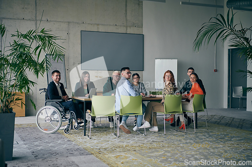 Image of A diverse group of business professionals, including an person with a disability, gathered at a modern office for a productive and inclusive meeting.