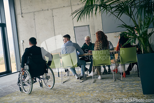 Image of A diverse group of business professionals, including an person with a disability, gathered at a modern office for a productive and inclusive meeting.