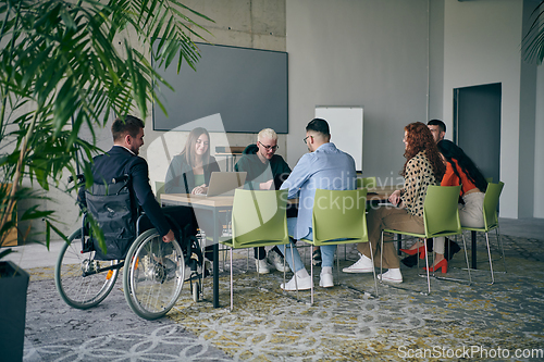 Image of A diverse group of business professionals, including an person with a disability, gathered at a modern office for a productive and inclusive meeting.